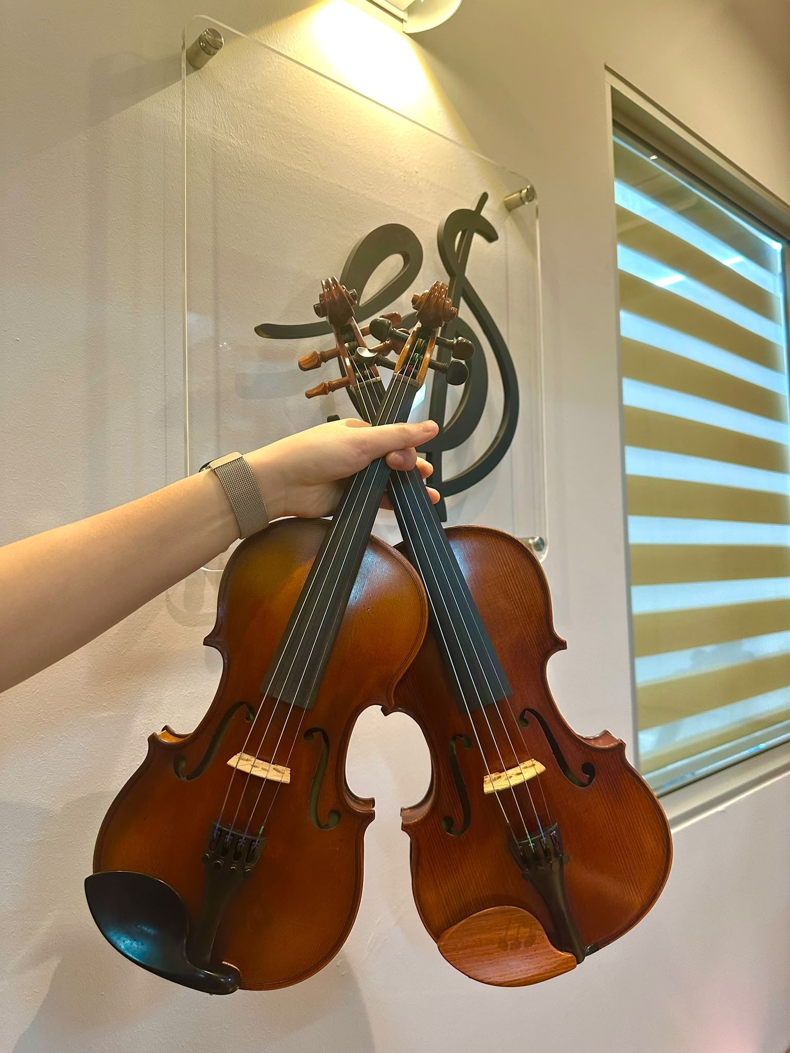 Two rental violins held up in front of the Bowed Strings Music Studio logo